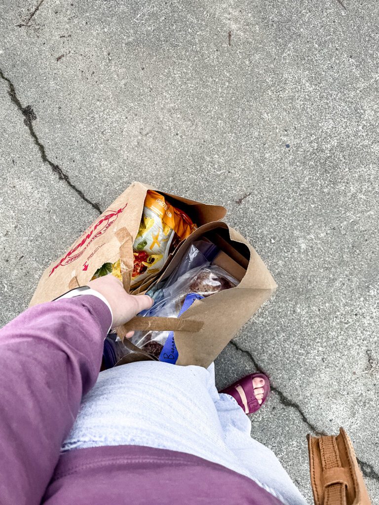 Photo taken from shoulder height facing towards the ground. An image of a hand holding two bags full of food. 