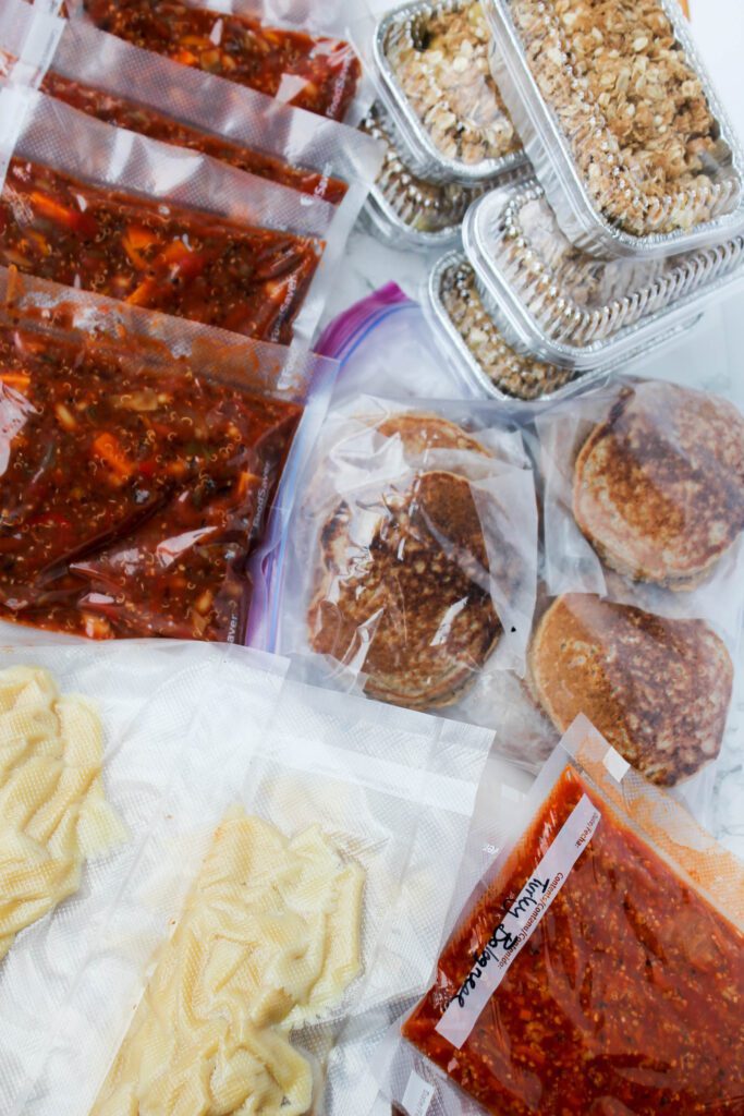 Sealed and packaged foods in vacuum seal bags. Bags are full of pancakes, pasta, and chili all laid out on top of a countertop.