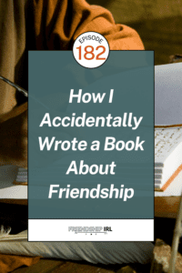 Friendship IRL podcast promotional graphic for Episode 182. The background features a warm, moody photo of an open journal or notebook resting on a wooden surface beside a stack of books, with a person wearing an orange/rust-colored garment visible in the soft-focus upper background, suggesting a cozy writing or reading setting. Overlaid in the center is a teal-blue semi-transparent rectangle with large bold white italic text reading "How I Accidentally Wrote a Book About Friendship," topped by a white circular badge with the text "EPISODE 182" in black and orange. At the bottom of the graphic, a white footer bar displays the "FRIENDSHIP IRL" podcast logo in bold black text alongside small audio player icons.
